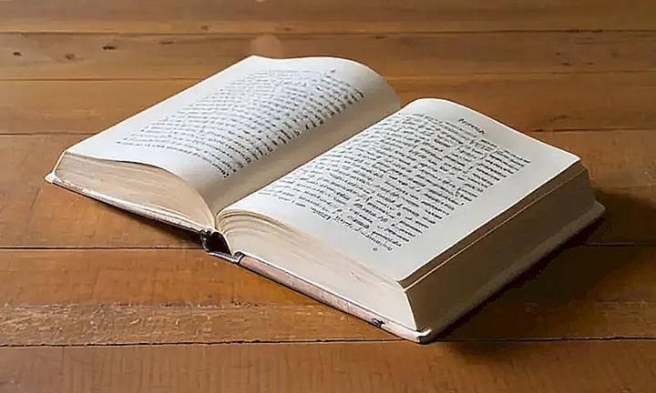 Un libro de tapa blanca desgastada está abierto sobre una mesa antigua