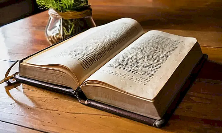 Un libro de estudio de ciudadanía española se abre sobre una mesa de madera, rodeado de flores frescas y un lápiz abandonado