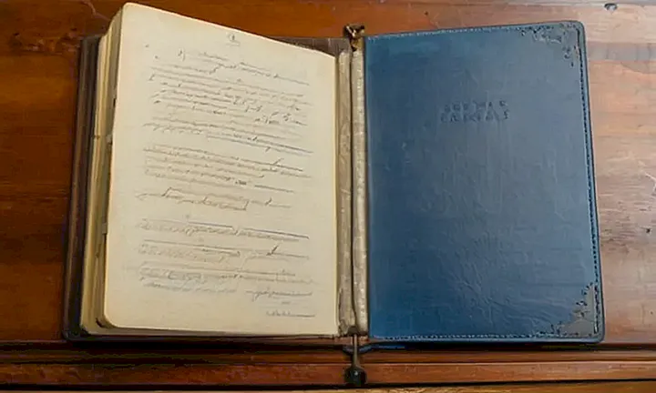 En una mesa desordenada hay un folio gastado con papeles amarillentos y un bolígrafo quebradizo
