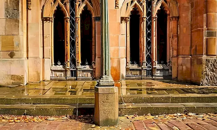 La fachada de una iglesia medieval, desgastada pero ornada, se inclina ligeramente sobre el acera de un callejón empedrado