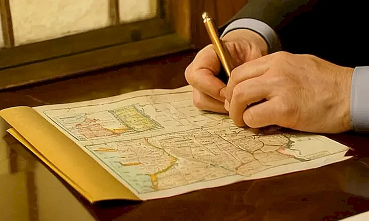Una persona siente nostalgia mientras revisa un antiguo documento en su oficina iluminada y observa una mapa de España detrás de ella