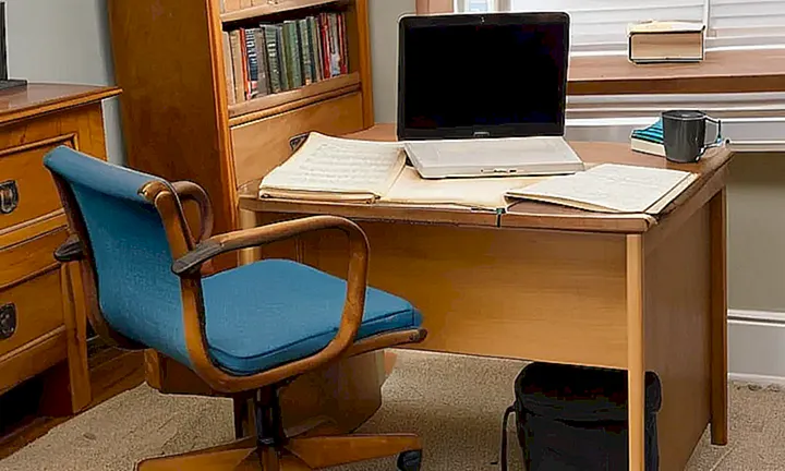 El escritorio está lúcidamente iluminado y rodeado de libros y papeles con un ordenador en la pantalla