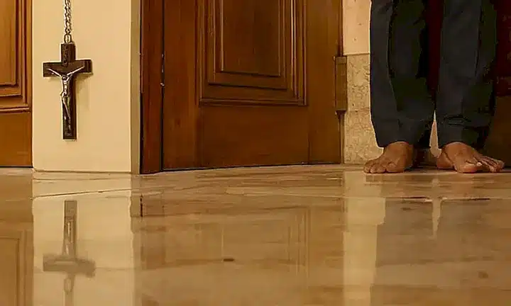 Una persona de origen brasileño se encuentra frente a un gran muro con una puerta antigua ornamentada en un espacio iluminado por una luz débil