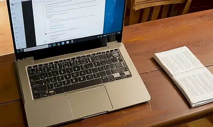 Una persona está sentada en una mesa de madera con un portátil abierto, llenando una declaración electrónica con la luz del sol natural iluminándolo todo