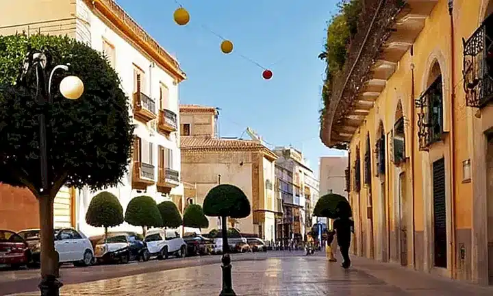 Una calle española en Valencia presenta un escenario sereno y animado con edificios históricos rodeados de árboles y la vida cotidiana