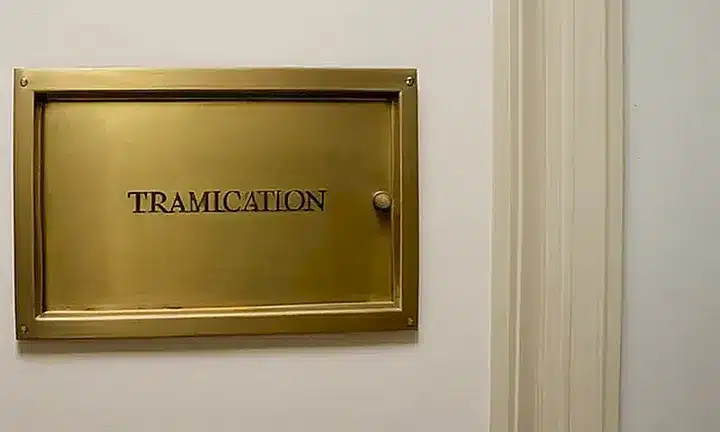 Una puerta beige con una cerradura de latón está flanqueada por dos ventanas con vidrio opaco y marcos de aluminio en un rincón oscurito