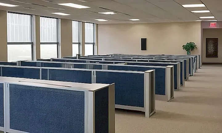 La sala de espera de un despacho tiene un suelo azul oscurecido y paredes beige con pósteres descoloridos bajo una luz fluorescente tenue