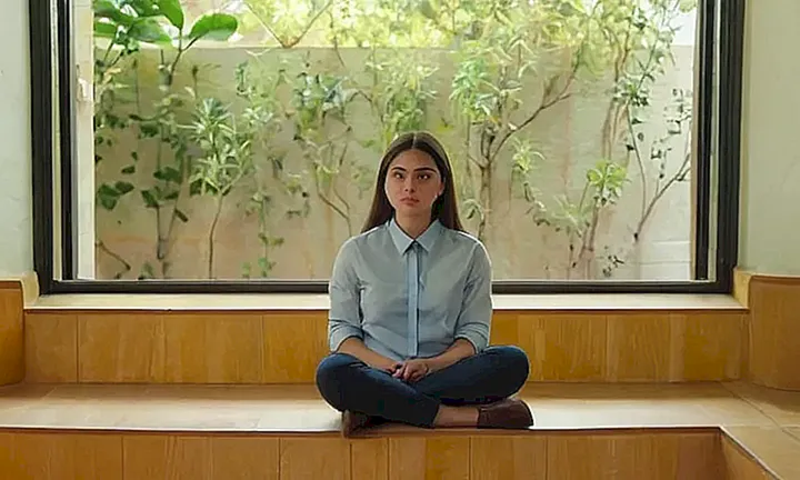 La imagen muestra un joven en una clase universitaria con luz natural y escuchando atentamente sus notas mientras se encuentra rodeado de elementos decorativos en la pared