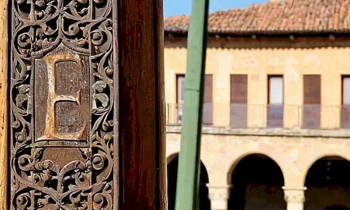 Un viejo cartel colgando de un poste de madera desgastada bajo una sombra, mostrando las huellas del tiempo en su tela