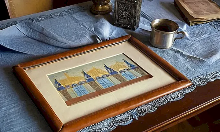 En la habitación hay un antigua mesa con detalles intrincados iluminada por una bombilla y rodeada de objetos personales del anciano