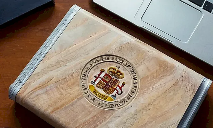 En una mesa de madera oscura se encuentran documentos atados y un ordenador portátil con una pantalla que muestra Descubre... parcialmente cubierta por un cúter oxidado