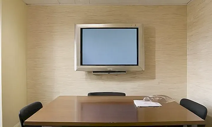 La habitación es una oficina sencilla con paredes de yeso beis, techos fluorescentes y un televisor que muestra una pantalla azulada