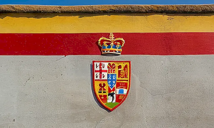 Una bandera española gotea sobre una pared de concreto grises y desgastada, adornada por la suave luz del sol poniente