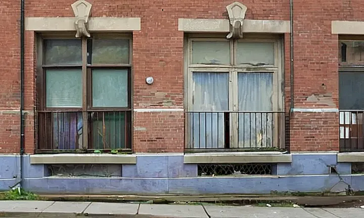 Un edificio gubernamental desgastado de color grisáceo-azulado y su pared lateral están rodeados por un raro escenario urbano