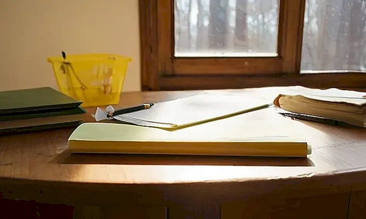 Un mueble de madera antigua con un libro abierto cubierto de papel y objetos está rodeado por siluetas oscuras en una habitación suavemente iluminada