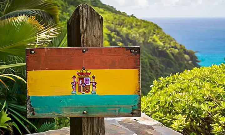 Un viejo poste de madera con una inscripción española desvaída se encuentra entre el follaje tropical en las Antillas
