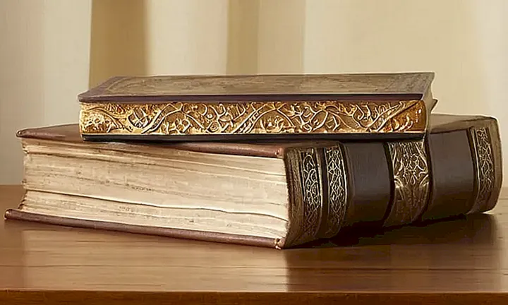La imagen muestra una pedestral de piedra weatherizada con dos libros antiguos y ornamentados sobre un fondo amarillento que evoca el barniz antiguo