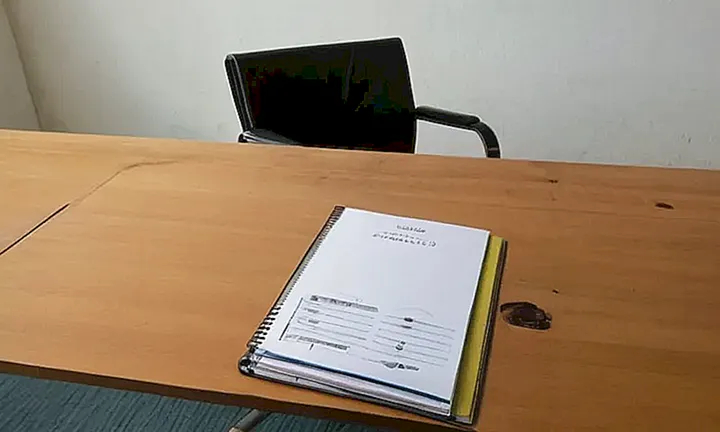 Una mesa de madera con una carpeta abierta y un portahojas descansan en la oficina bajo luz fluorescente