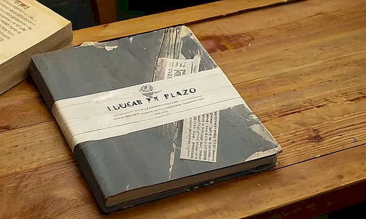 Sobre un escritorio desordenado descansa una cubierta de informe en papel con título digital parcialmente gastado y pegada con cinta adhesiva