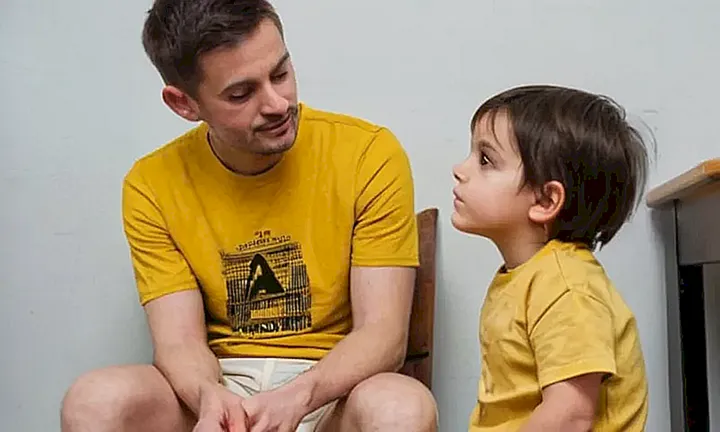 Un niño de 4 años se sienta en el piso con una expresión calmada y un adulto sentado frente a él, tomando su mano delicadamente