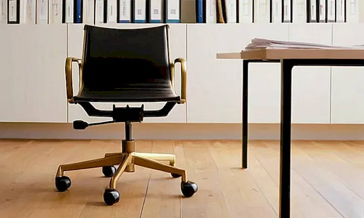 Una persona está sentada en una silla ergonómica moderna revisando un documento oficial en una sala minimalistamente amueblada