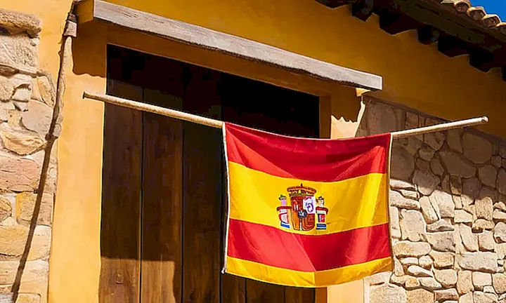 La bandera española cuelga perfectamente al centro de un muro amarillo viejo bajo la suave luz matinal