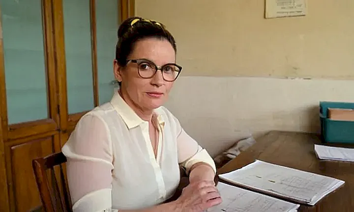 Una mujer vestida con una camisa blanca va a trabajar en un escritorio desgastado de madera en un edificio municipal decrépito