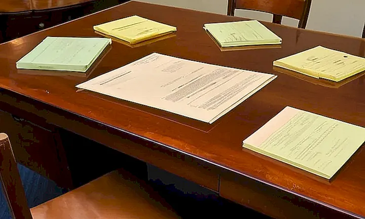 Una mesa con un mantel de lino desgastado está decorada con importantes documentos y materiales de escritorio ordenados cuidadosamente en una atmósfera de oficina oscura