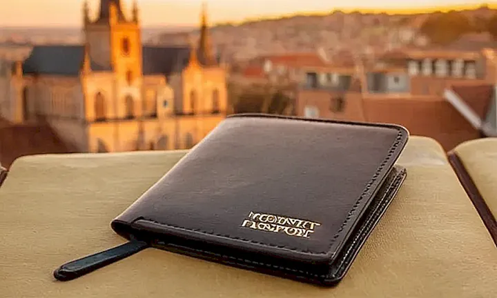 La imagen muestra un pasaporte español abierto sobre un fondo borroso de la ciudad belga al atardecer