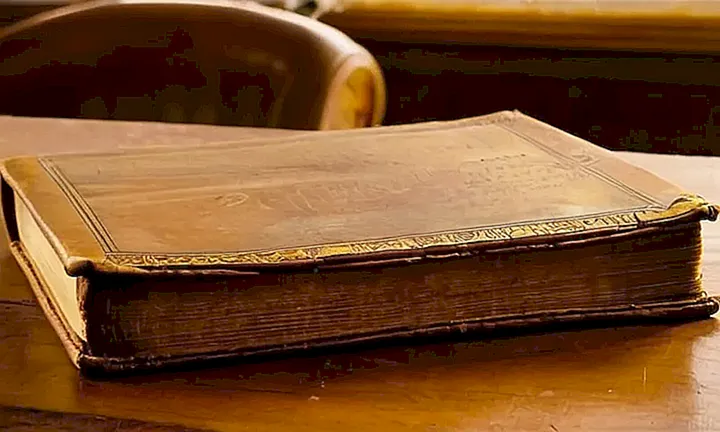 Un viejo libro de cuero descansa sobre una mesa tallada con luces suaves que se filtran a través de ventanas sucias