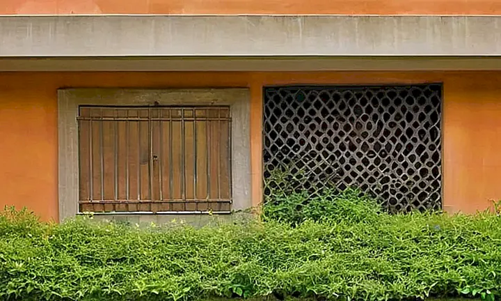 La descripción detalla un exterior desgastado de una antigua estructura con detalles como banderolas rasas y vidrios distorsionados, rodeada por vegetación exuberante con profundidad visual creada por luces y sombras