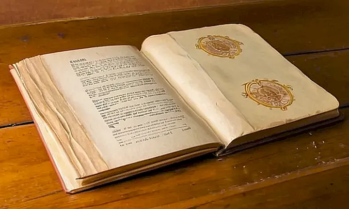 Un antiguo libro de tapas off-white, con logotipo y texto de una organización gubernamental, aparece sucio en la superficie de un escritorio desordenado