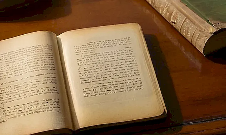 Un libro de tapa amarillenta y desgastada está abierto sobre un escritorio cubierto con detalles y la luz del sol hace que el polvo flote en el aire
