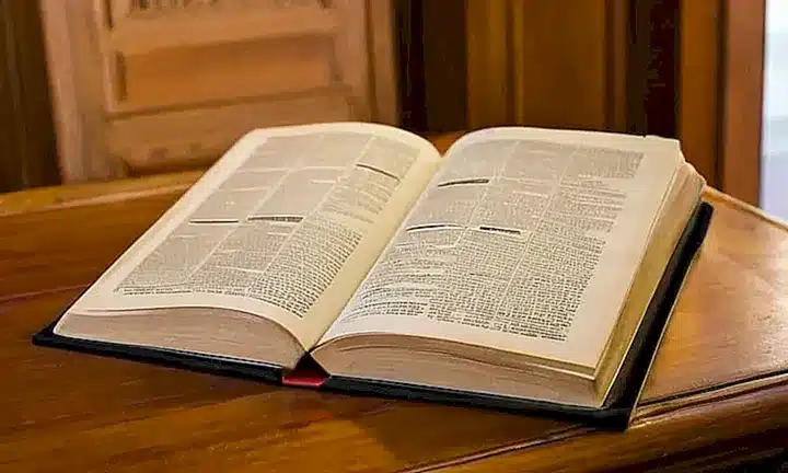 Una página de un libro antiguo, iluminada por la luz dorada de una ventana, muestra detalles minuciosos acerca de las leyes tributarias de España e Italia
