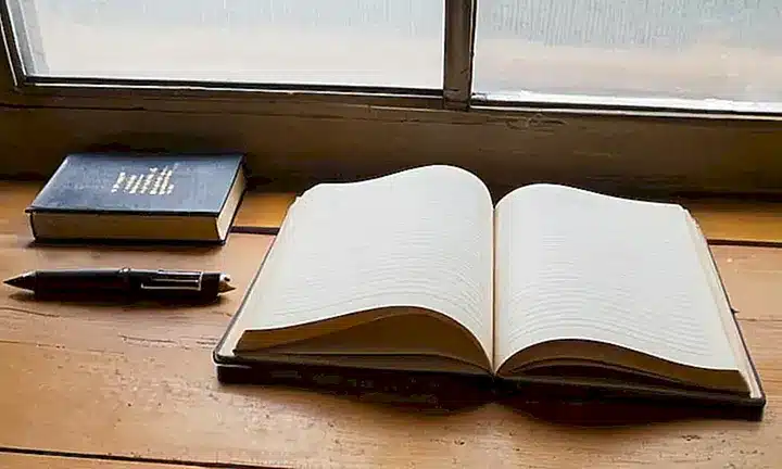 Un libro encuadernado de papel está abierto sobre una mesa desordenada con elementos antiguos