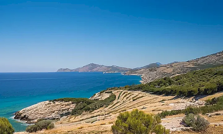 Una página A4 de papel con un patrón de líneas finas y el logotipo español en la parte superior, acompañada por una foto agradable de una costa mediterránea con colinas onduladas