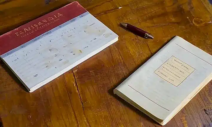 Se ve un libro desgastado y un antiguo escritorio deteriorado con muestras de uso y tiempo