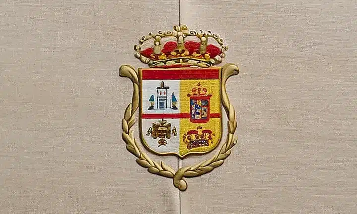 El objeto es una carpeta de color marrón oscuro con un emblema español y un fondo blanco desgastado