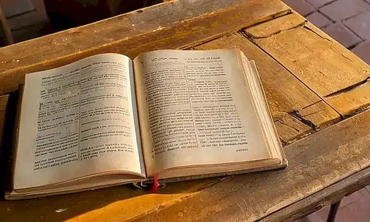 Un libro desgastado y un paño español descolorido se reflejan en una mesa de madera clásica bañada por suavísimos rayos de luz