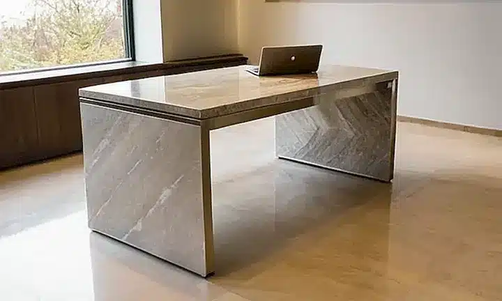 Una habitación de oficina tiene detalles en madera y mármol que reflejan la luz, al lado de objetos destacados como una foto del político y un libro encuadernado
