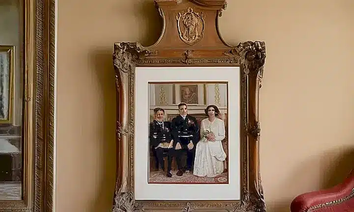 La escena muestra un anciana mesa de madera con una pareja de 1950s enmarcada al fondo detrás de ellos, familiares y objetos ornamentales que reflejan un pasado nostálgico
