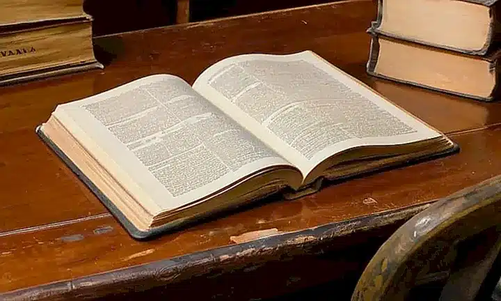 Una habitación con un escritorio lleno y una luz tenue se refleja en el conjunto de libros antiguos y tecnología moderna
