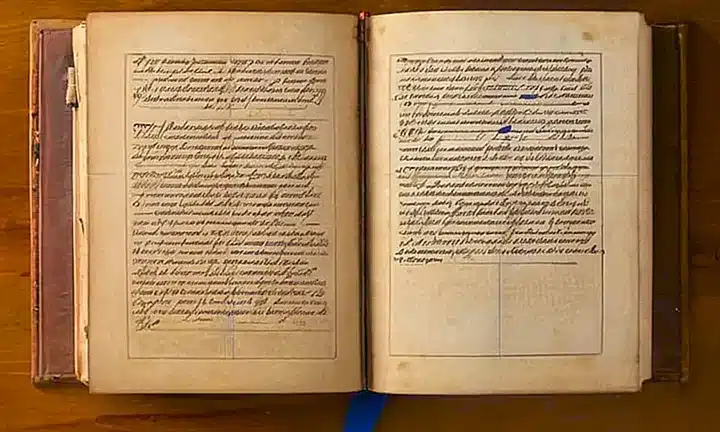 Un libro antiguo de cuero claro con páginas amarillentas y notas en el margen reposa sobre un escritorio desordenado