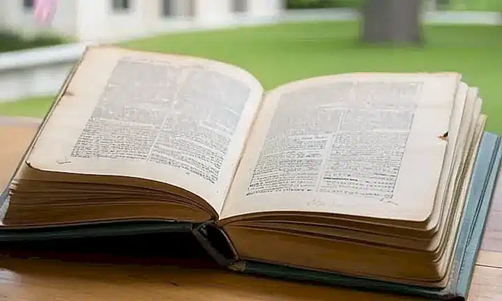 Una vieja Biblia descansa sobre una mesa de madera, rodeada del ambiente caluroso y tranquilo de una habitación interior con vistas vagas de la ciudad