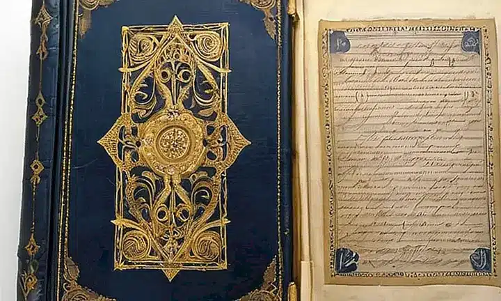 Un documento histórico antiguo de cuero azul oscuro se muestra a gran detalle con inscripciones en tinta negra sobre papel pergamino suave y descolorido