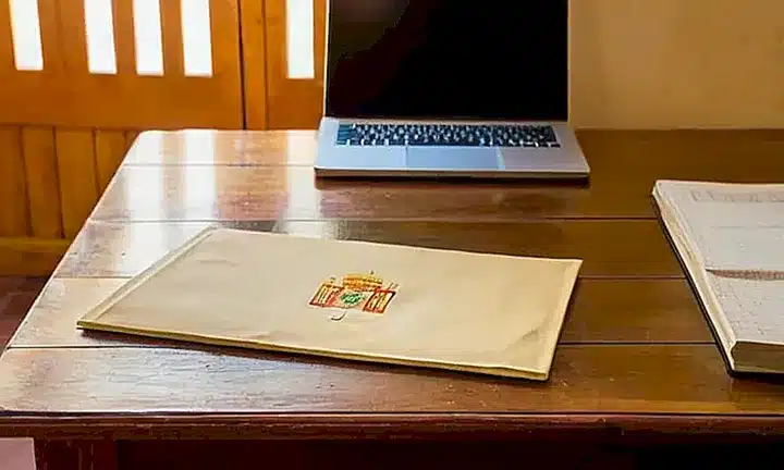 Una mesa desordenada muestra un antiguo texto español cubierto con una tapa rojiza, acompañado por otros elementos y objetos de deseo