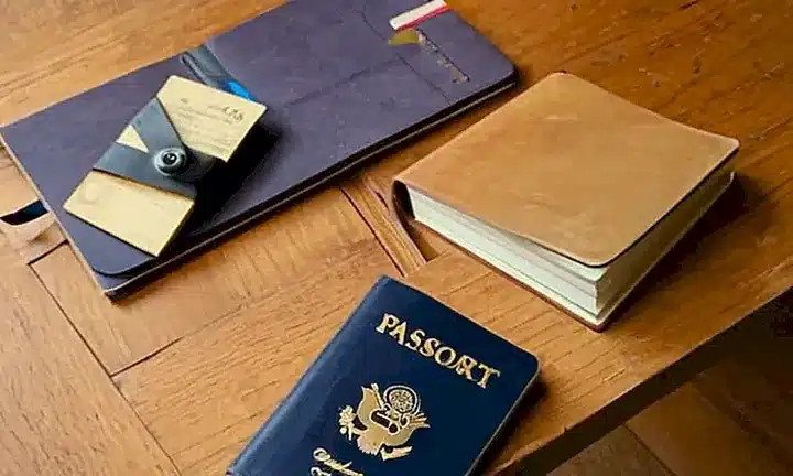 En una mesa de madera vencida están dispuestos un pasaporte desgastado y varios documentos amarillentos con notas escritas a mano