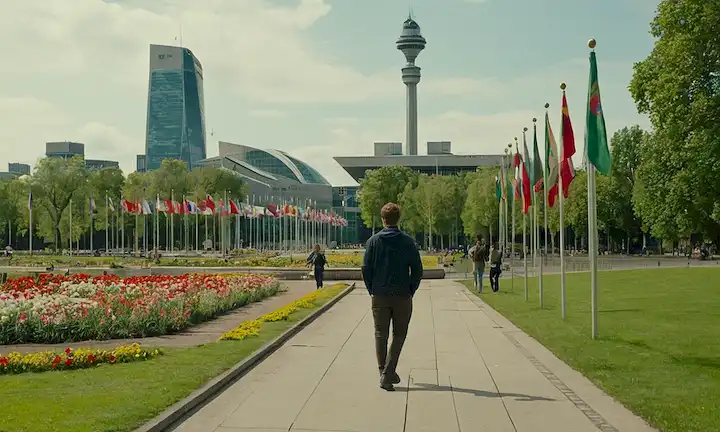 Una persona de pie frente a un paisaje urbano con edificios y calles, un edificio de gobierno en el fondo con banderas ondeando, un paisaje verde con árboles y flores, un aeropuerto o una estación de autobuses cerca, un mapa o globo sobre una mesa, personas de diferentes nacionalidades caminando juntos, un sutil toque de movimiento hacia la libertad