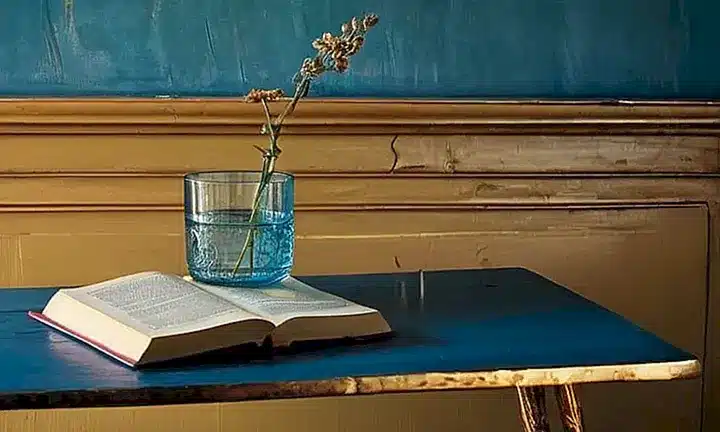 La habitación está iluminada por un rayo de sol que entra a través de una ventana sucia, destacando detalles como la portada embossed de un libro sobre una mesa antigua
