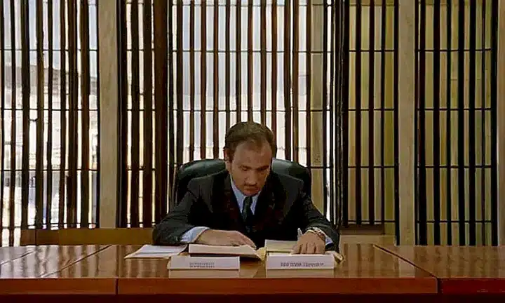 Una persona se sienta en un escritorio antiguo de una oficina gubernamental observando atentamente un formulario en su estado de deterioro